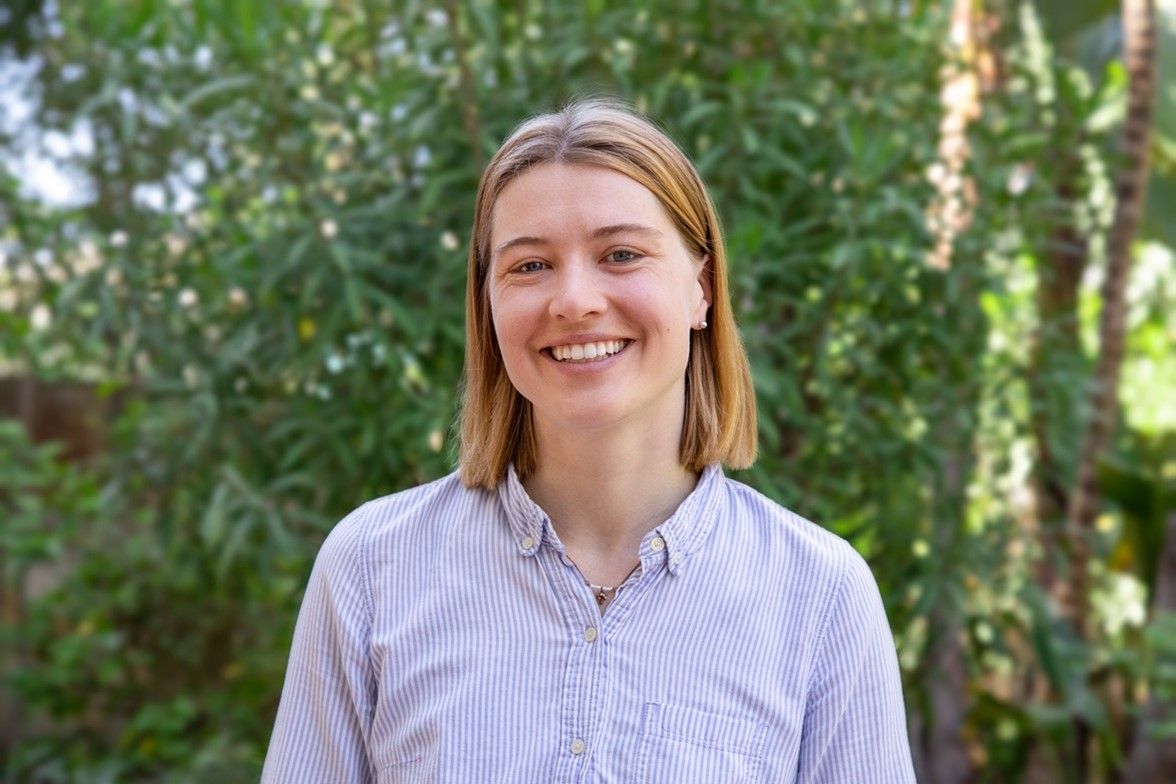 A white woman with blunt-cut blonde shoulder-length hair wears a blue collared shirt and smiles at the camera